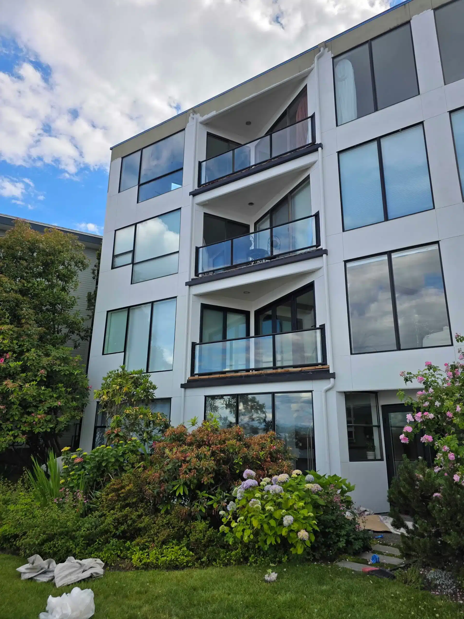 Modern Apartment Building Exterior Painting Exterior view of a modern white apartment building with large windows and glass balconies, surrounded by lush landscaping.