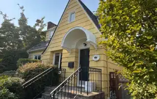 Golden yellow exterior residential home with dark roof, black entry door and arched portico, white-trimmed windows