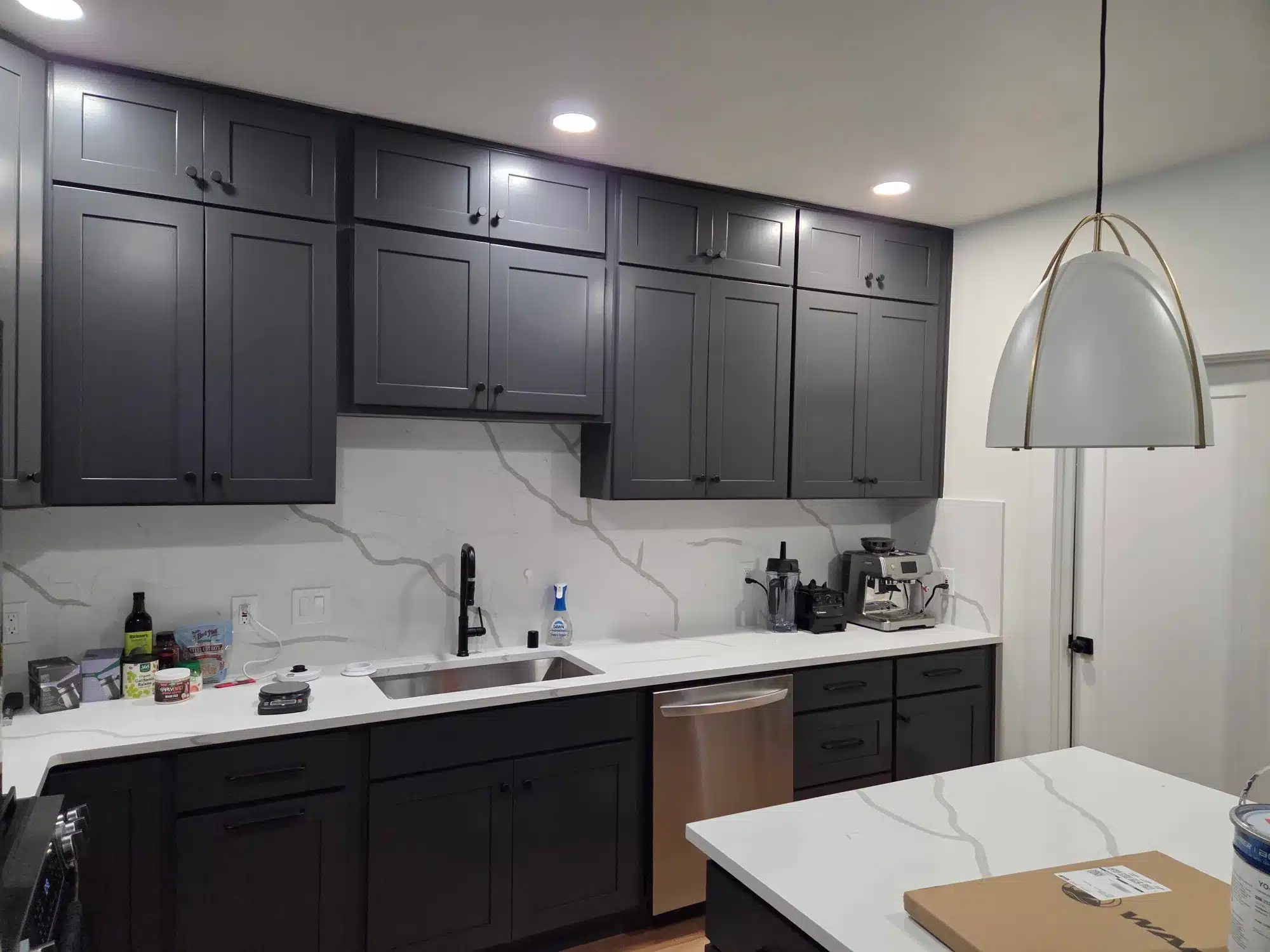 Black Painted Kitchen Cabinets Black painted kitchen cabinetry with white quartz countertop and marble backsplash in residential kitchen